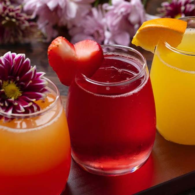 Three colorful drinks at Mi Guadalajara Restaurant, each garnished with fruit, on a wooden surface.