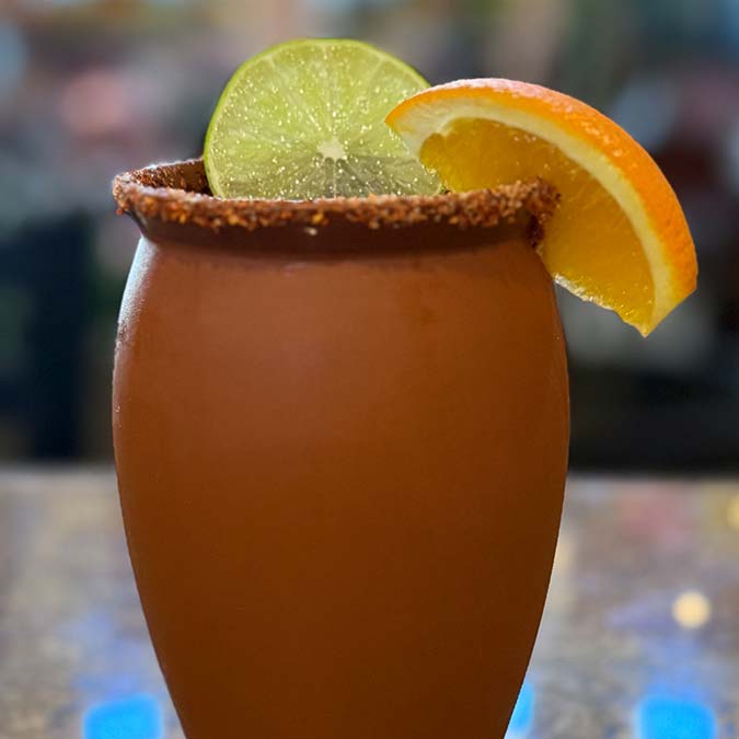 Clay cup with salt rim at Mi Guadalajara, citrus garnish, blurred Escondido background.