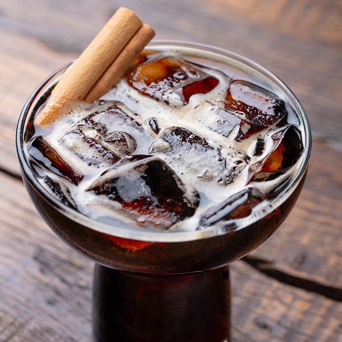 Glass of cola with ice cubes and a cinnamon stick beside tacos on a wooden table in Escondido.