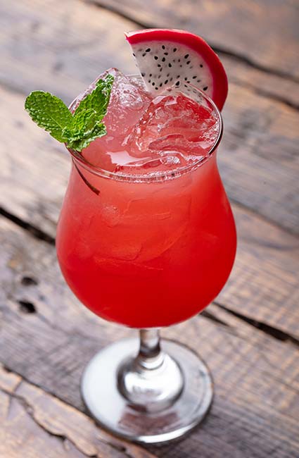Red cocktail with ice, mint, and dragon fruit at Mi Guadalajara Restaurant on a wooden surface.