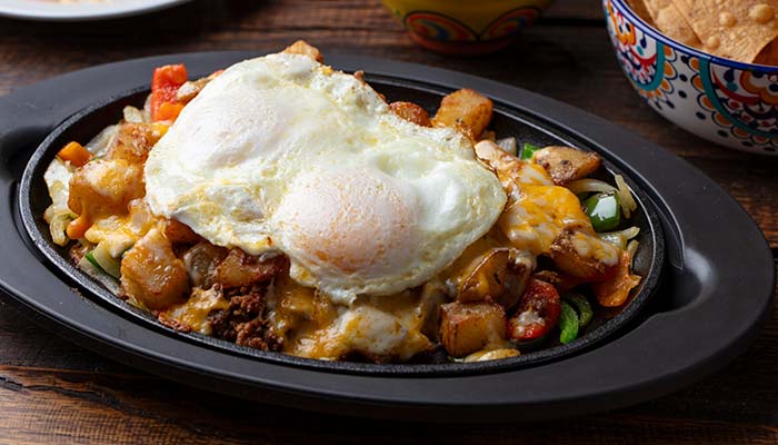 Two sunny-side-up eggs over hash browns, veggies, cheese—classic Mexican restaurant comfort.