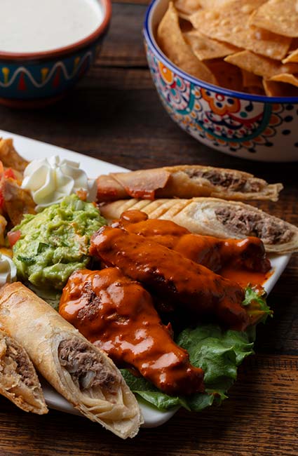 Plate with sauced wings, taquitos, guac, chips & dip from Mi Guadalajara Restaurant in Escondido.