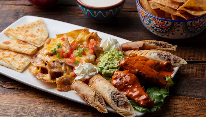 Platter with Mexican Food favorites: quesadillas, nachos, taquitos, wings, guac, and sour cream.
