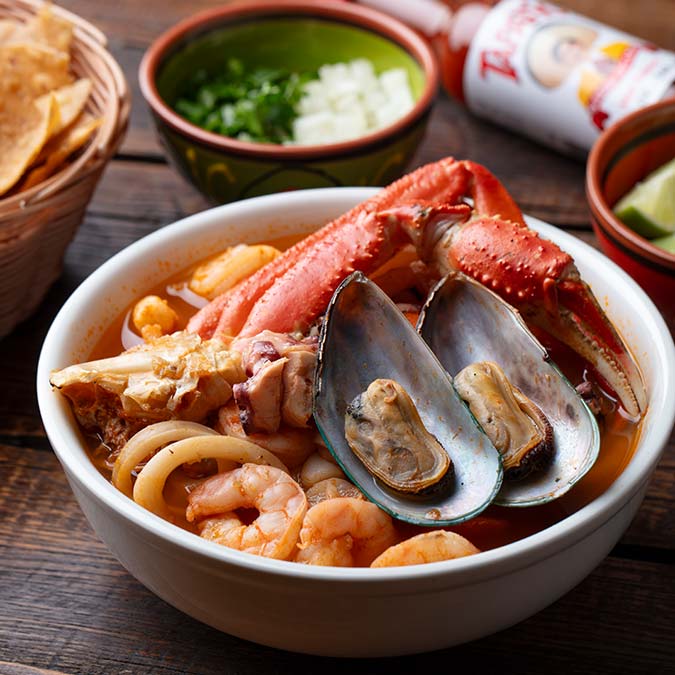 Seafood soup with shrimp, mussels, and crab claws from Mi Guadalajara Restaurant on a wooden table.
